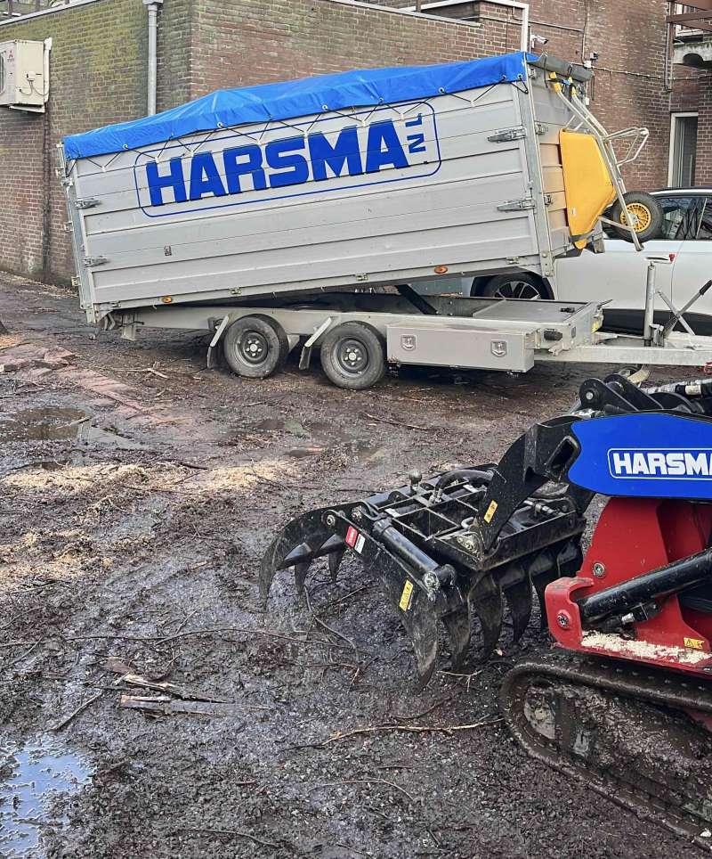 Aanhanger met rupsvoertuig, uitgerust met bomenklem. Werk in uitvoering op een parkeerplaats.