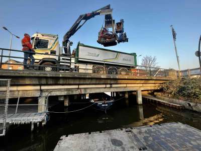 Rupsvoertuig + Maaiarm wat opgetild voor werkzaamheden aan een talud vanaf het water, op een ponton.