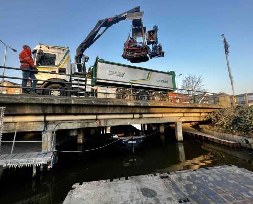 Rupsvoertuig + Maaiarm wat opgetild voor werkzaamheden aan een talud vanaf het water, op een ponton.