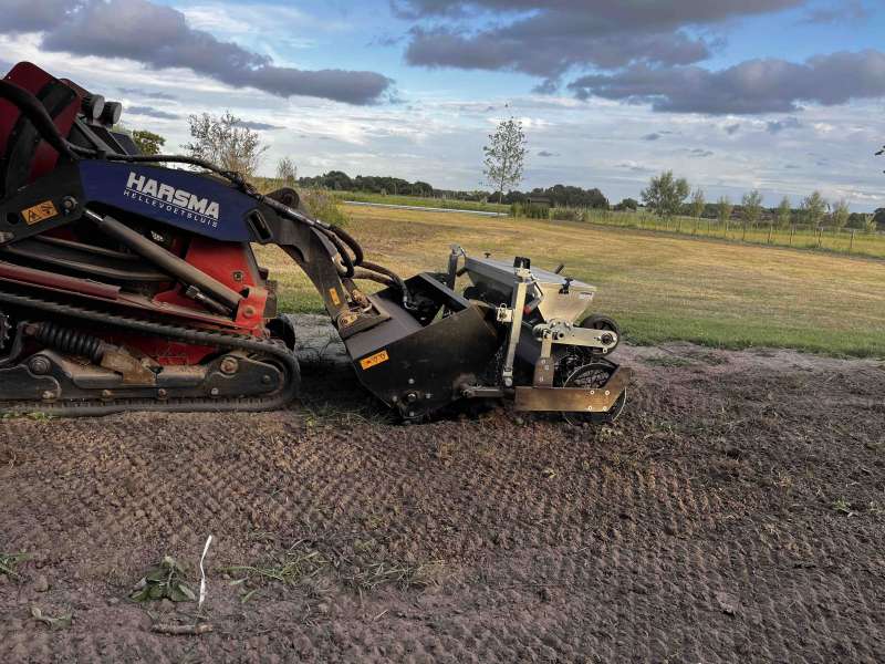 Rupsvoertuig uitgerust met een graszaaimachine, tijdens het uitvoeren van zijn werkzaamheden.