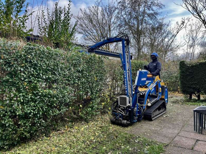 Snoeien van een haag, met een smal rupsvoertuig op een locatie op Texel